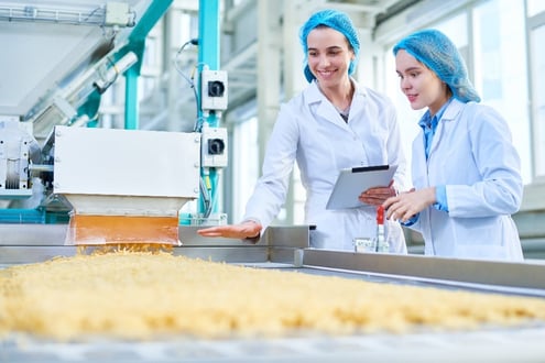 Two women in lab cotes in a factory analyzing a product 